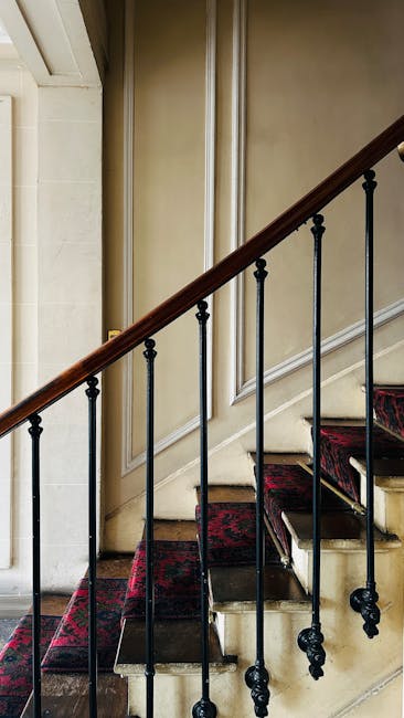A staircase inside a property with wooden steps and white risers, leading up to a small landing near a window with multiple panes, which is framed by dark wood trim. Several potted plants, including a